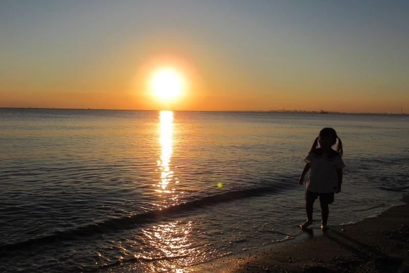 子どもが海に映る夕日を見つめる様子